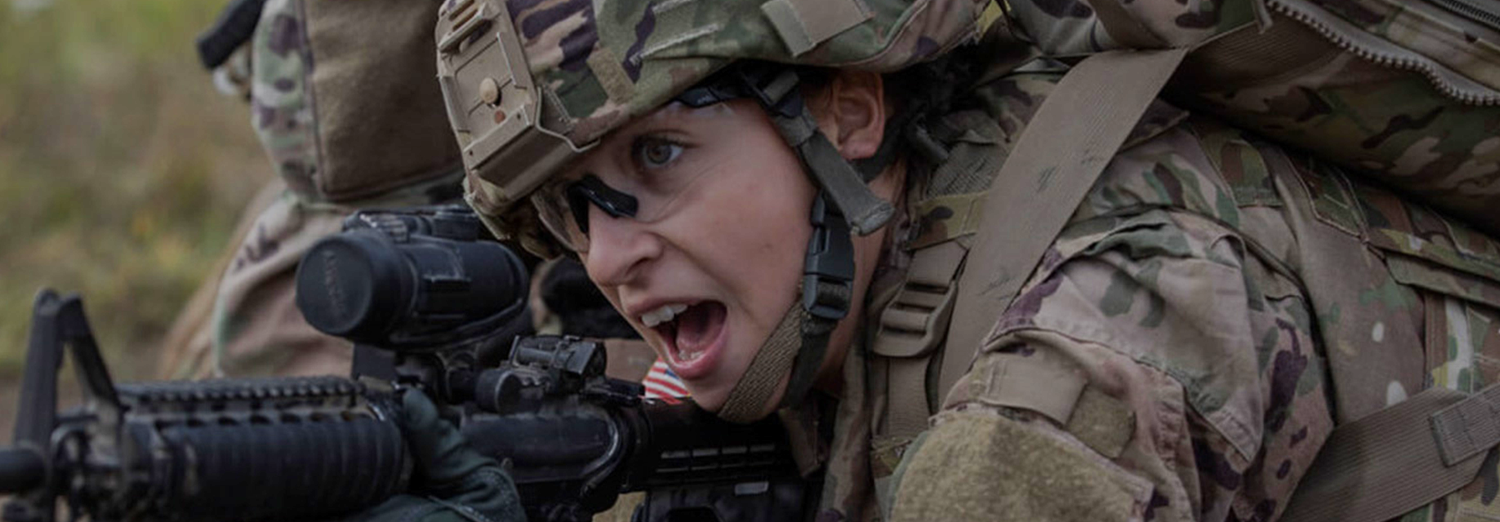 Female soldier aiming a weapon while looking through the scope.