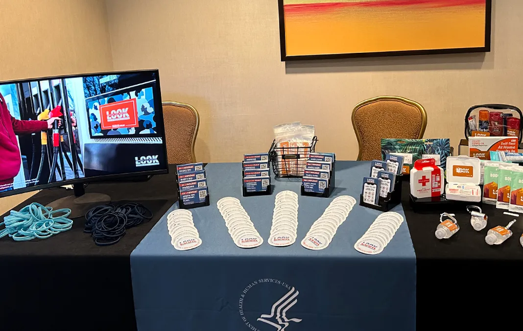 Merchandise for the Look Beneath the Surface campaign displayed on a table featuring stickers, bracelets, business cards, mini first aid kits, and hand sanitizer keychains.